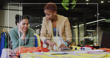 Measuring designer in blazer inspecting orange fabric at design studio, with colleague and tools. Creativity, craftsmanship, collaboration, workspace, patterning, innovation, fashionの写真素材