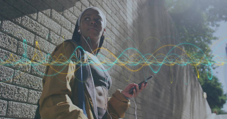 Leaning sporty woman holding smartphone listening through earphones on sunlit sidewalk, sound waves....