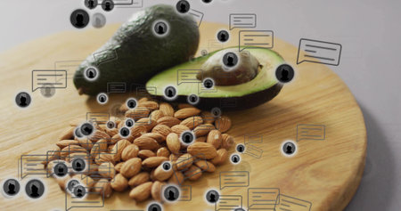 Displaying halved avocado, whole avocado, almonds on cutting board on table, with floating icons. Healthy snack, digital communication, modern design, wellness, natural, minimalism, food presentationの写真素材