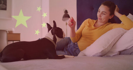 Adult woman reclining and touching small dog on bed in bedroom, with yellow star shapes. Lifestyle, comfort, relaxation, cozy, tranquility, contemporary, domesticの写真素材