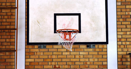Displaying basketball backboard and rim hanging on brick wall in gym, with net and ladder. Sports, recreation, urban, vibrant, athletic, fitness, trainingの写真素材