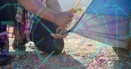 Kneeling flannel hiker inserting tent pole into fabric on gravel ground, securing stake with boots. Adventure, teamwork, outdoor, rugged, exploration, collaboration, resilienceの写真素材
