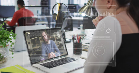 Turning woman facing laptop showing man talking in modern office, with plant, notebook, copy space. Professional, modern, collaborative, technology, workspace, productivity, sleekの写真素材