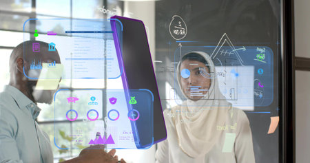 Professionals wearing hijab collaborating in office, with glass panel displaying holographic charts....