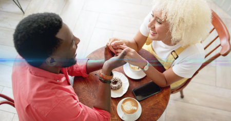 Leaning couple holding hands at cafe table, with latte art cups, doughnut and smartphone. Romance, intimacy, companionship, cozy, warm, social, lifestyleの写真素材