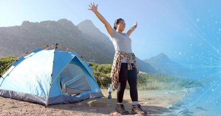 Woman in hiking gear raising arms on mountain campsite, with dome tent, water bottle, copy space....