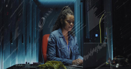 Monitoring woman wearing denim working on laptop in server room, network cables and circuit boards....