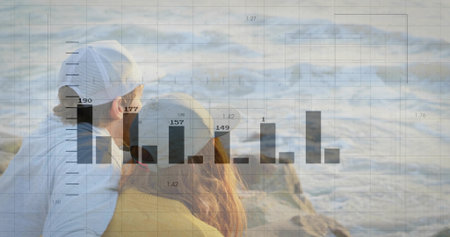 Sitting couple wearing caps and mustard sweater on sandy beach watching waves. Romantic, relaxation, tranquility, coastal, leisure, nature, harmonyの写真素材