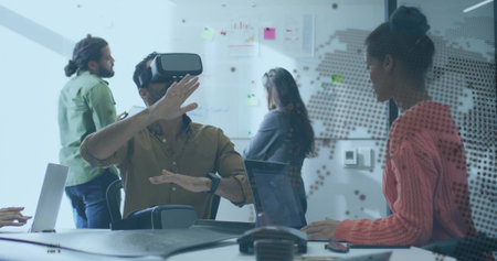 Man wearing VR headset making hand gestures in meeting room, with laptops, conference phone....