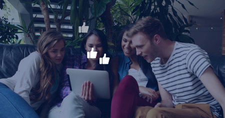 Leaning friends viewing tablet on leather couch in lounge with plants, floating thumbs-up graphics....