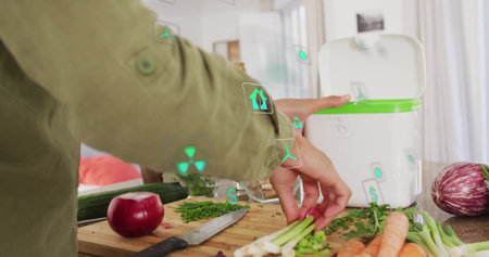 Home cook in green jacket lifting vegetable scraps into green-rim compost bin on kitchen counter. Grocery, sustainable, culinary, minimalist, eco-friendly, household, organicの写真素材