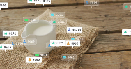 Showing white ceramic milk pitcher on burlap cloth on wooden table with floating reaction icons....