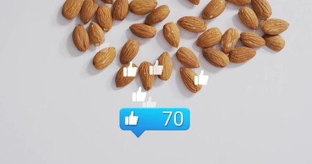 Showcasing unroasted almonds resting on studio desk, floating thumbs up icons and blue like bubble. Nut, health, minimalist, digital, social media, technology, wellnessの写真素材