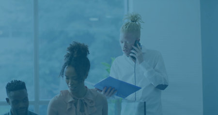 Discussing documents, three coworkers leaning over desk in office, with smartphone and blue folder. Collaboration, teamwork, brainstorming, professional, urban, modern, corporateの写真素材