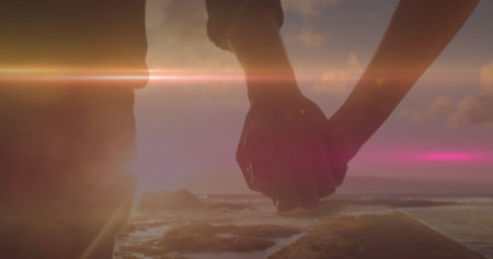 Holding hands woman and man standing on narrow pier at ocean sunset, wearing casual summer clothes. Romance, silhouette, serenity, landscape, dusk, connection, harmonyの写真素材
