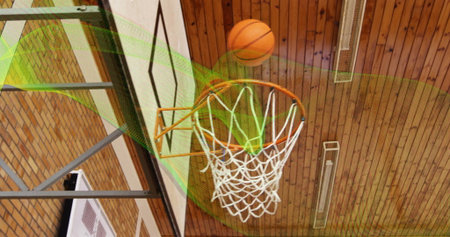 Passing orange basketball through metal rim and net inside gymnasium with backboard, lights. Sports,...
