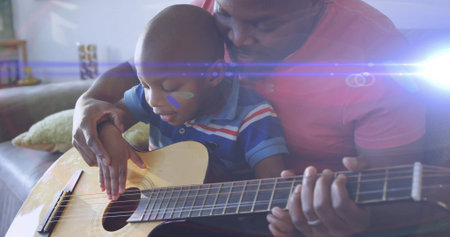 Strumming father and son playing acoustic guitar on couch at home, with decorative pillow, shelf....