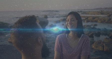 Sitting Hispanic couple wearing purple T-shirt and casual top on rocky shore at sunset, copy space. Coastline, leisure, natural, contemplative, serenity, friendship, picturesqueの写真素材