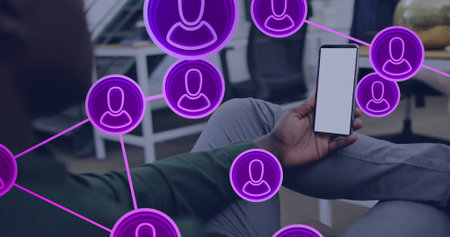 Sitting man holding smartphone in office lounge, with white screen and purple network icons. Technology, networking, communication, coworking, modern, professional, digitalの写真素材