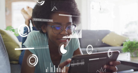 Analyzing charts student lying on sofa at home holding tablet, with pillows by coffee table plant. Automation, education, digital, innovation, relaxation, technology, homeの写真素材