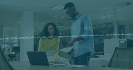 Two office colleagues wearing business attire reviewing documents at office desk, with laptop. Collaboration, teamwork, data analysis, professional, modern, corporate, productivityの写真素材