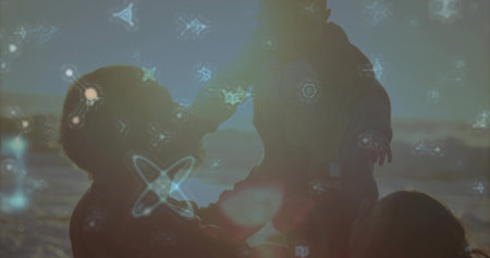 Family silhouette lifting baby on shoreline at sunset, with mom watching, knit hat and hoodie. Sunset, silhouette, family, beach, water, horizon, warmの写真素材