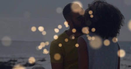 Kissing couple wearing summer attire on sandy shore, with ocean waves horizon line and bokeh lights. Romance, intimacy, affection, summer, leisure, serenity, connectionの写真素材