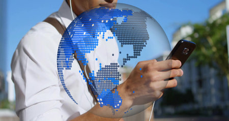 Man wearing white shirt earphones and bag checking smartphone on sunlit sidewalk with globe overlay....