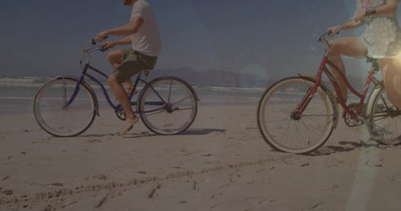 Cruising couple pedaling blue and red cruiser bikes along beach near water's edge, with ocean waves. Romantic, leisure, coastal, adventure, scenic, outdoor, vibrantの写真素材