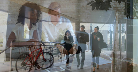 Two colleagues pointing at documents and typing on laptop at office desk, with red bicycle rack. Collaboration, professional, modern, workspace, urban, productivity, teamworkの写真素材