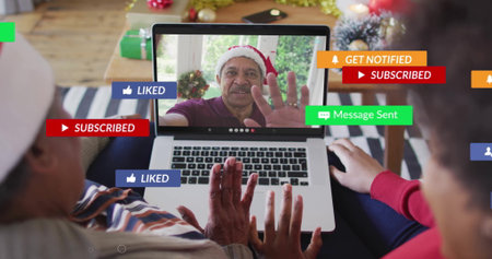 Waving senior and mid-adult women using laptop in decorated living room, with Santa hats and gifts. Festive, multi-generational, cozy, family, celebration, holiday, digitalの写真素材