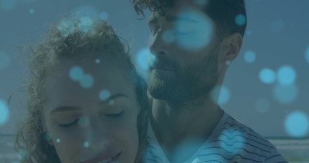 Standing couple wearing striped T-shirt and casual top at sandy beach, with soft blue light circles....