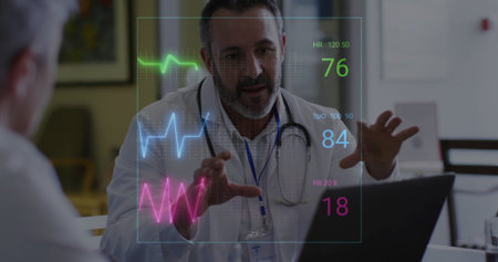 Gesturing doctor wearing coat, stethoscope consulting at clinic desk with laptop and vital graphs....