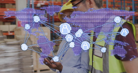 Two men wearing helmets and vests consulting handheld tablet in warehouse with global map overlay....