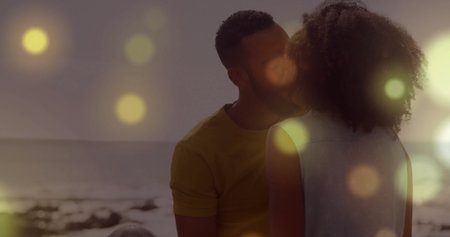 Kissing couple sitting on sandy beach at sunset, with gentle waves lapping and light flares. Romance, intimacy, sunset, serenity, nature, warmth, connectionの写真素材