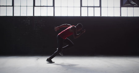Launching male athlete sprinting across warehouse floor, with red sports top, black tights. Performance, athleticism, speed, fitness, industrial, training, motivationの写真素材