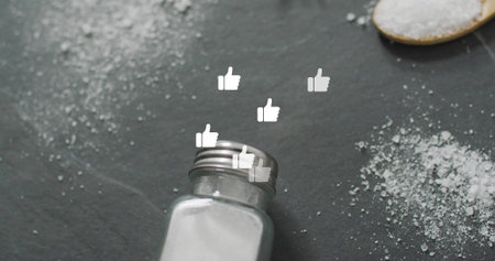 Tipping salt shaker spilling salt on kitchen countertop, with wooden spoon of salt, thumbs-up icons. Culinary, seasoning, minimalist, food styling, gastronomic, social media, approvalの写真素材