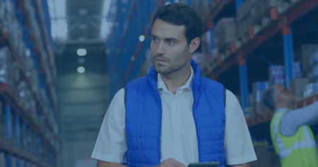 Warehouse supervisor holding tablet while inspecting pallet racks in aisle, under LED lights....