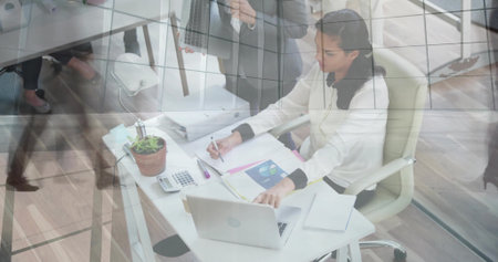 Writing Middle Eastern woman jotting data on notepad at modern office, with printed charts. Professional, workspace, modern, minimalist, corporate, collaboration, organizationの写真素材