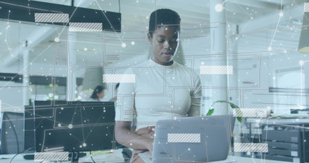 Analyzing IT professional interacting with laptop at modern open plan office, with digital overlays. Technology, workspace, digital, innovation, collaboration, modernity, dataの写真素材