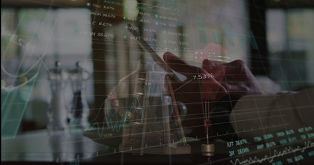 Holding smartphone above laptop keyboard at desk, displaying chart overlays. Technology, finance, analytics, modern, workspace, professional, digitalの写真素材