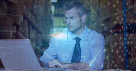 Working man in business attire using laptop at warehouse aisle, shelving racks and digital overlay. Industrial, logistics, technology, data, connectivity, infrastructure, efficiencyの写真素材