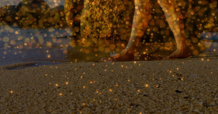Walking male legs and feet wading along pebbly beach with gentle waves, golden bokeh, copy space. Beach, coastline, serenity, natural, leisure, outdoor, tranquilityの写真素材