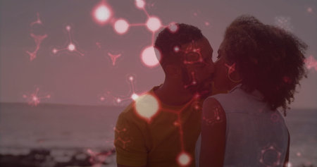 Kissing couple wearing denim vest and yellow T-shirt on rocky beach at sunset, floating red overlay. Romantic, serenity, outdoor, nature, tranquil, affection, warm-tonedの写真素材