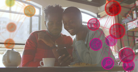 Couple wearing red shirt and denim jacket checking smartphone at cafe, with digital network graphic....