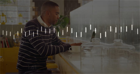 Man wearing striped sweater working on laptop at coffee shop counter, with cup and glass canisters....