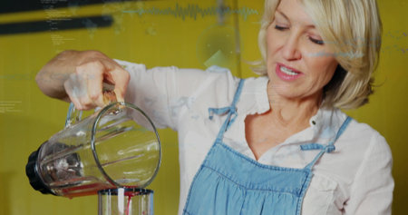 Home cook wearing denim apron pouring red smoothie from blender into container at kitchen counter. Cooking, culinary, kitchenware, lifestyle, modern, vibrant, healthの写真素材
