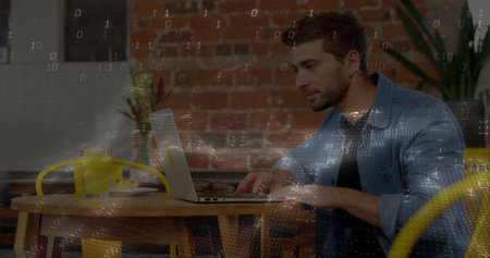 Typing man in denim shirt working on laptop at wooden cafe table, with yellow headphones, plants....
