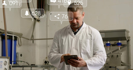 Lab coat technician using tablet in plant, with pipes, cables, notifications, blue filter housings....