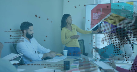 Gesturing woman in yellow cardigan presenting slide in office meeting room, with printed documents....